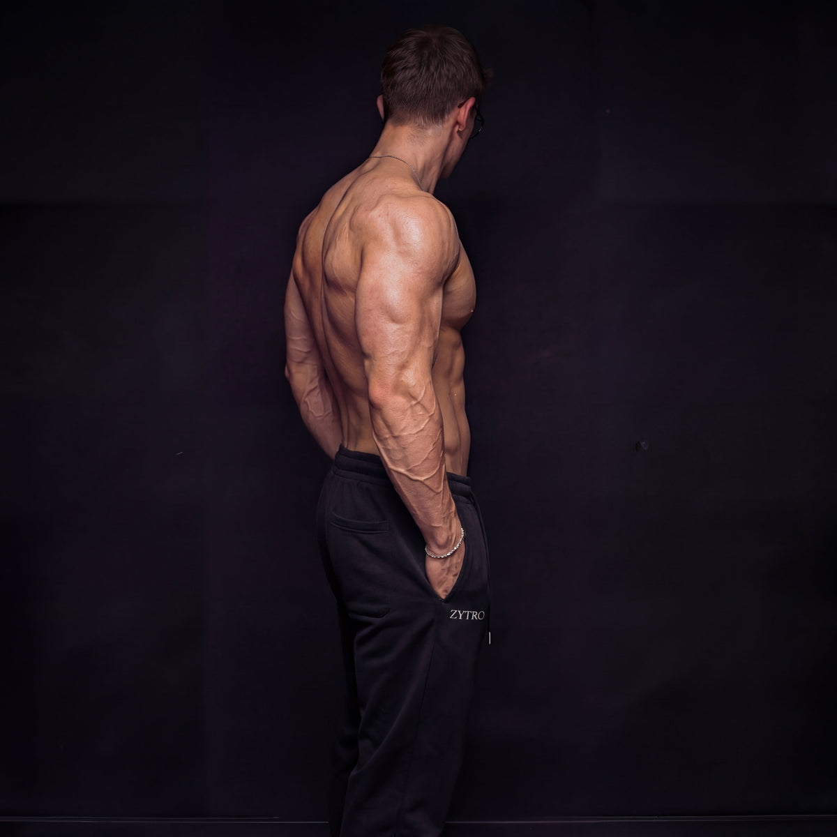 Muscular man standing against a black background wearing black pants with visible ZYTRO branding on left leg.